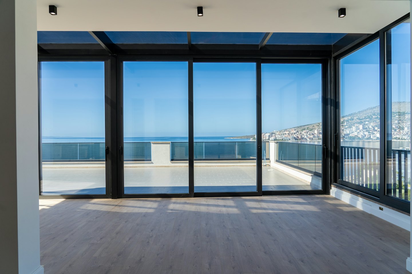 Chambre moderne vide avec portes vitrées donnant sur une ville côtière.
