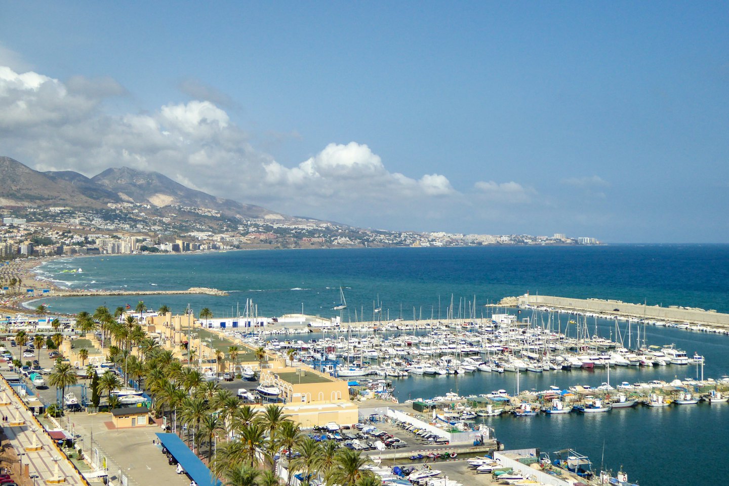 Ville côtière avec un port de plaisance animé et une plage de sable.